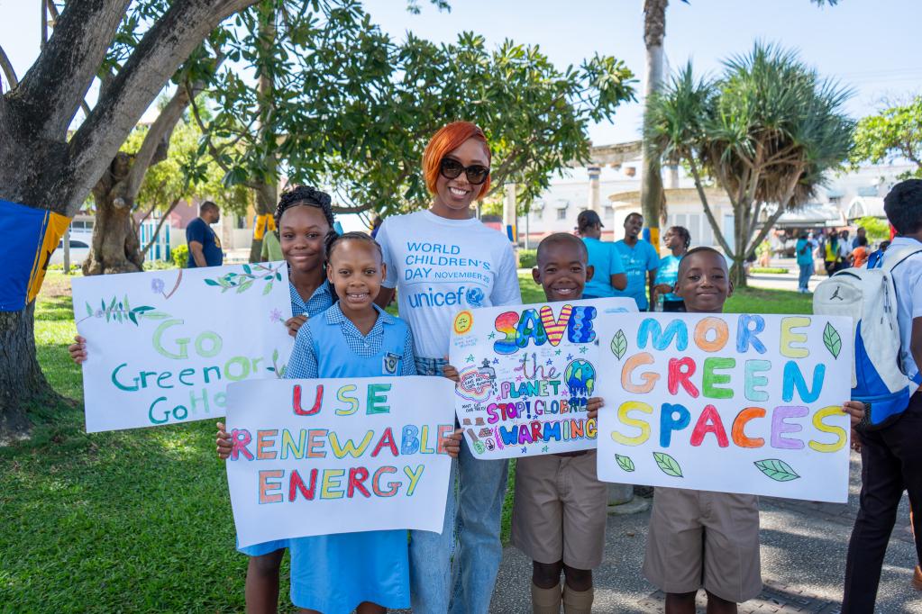 two young girls and two young boys in school uniforms with artistic climate posters stand with a smiling young woman in sunglasses