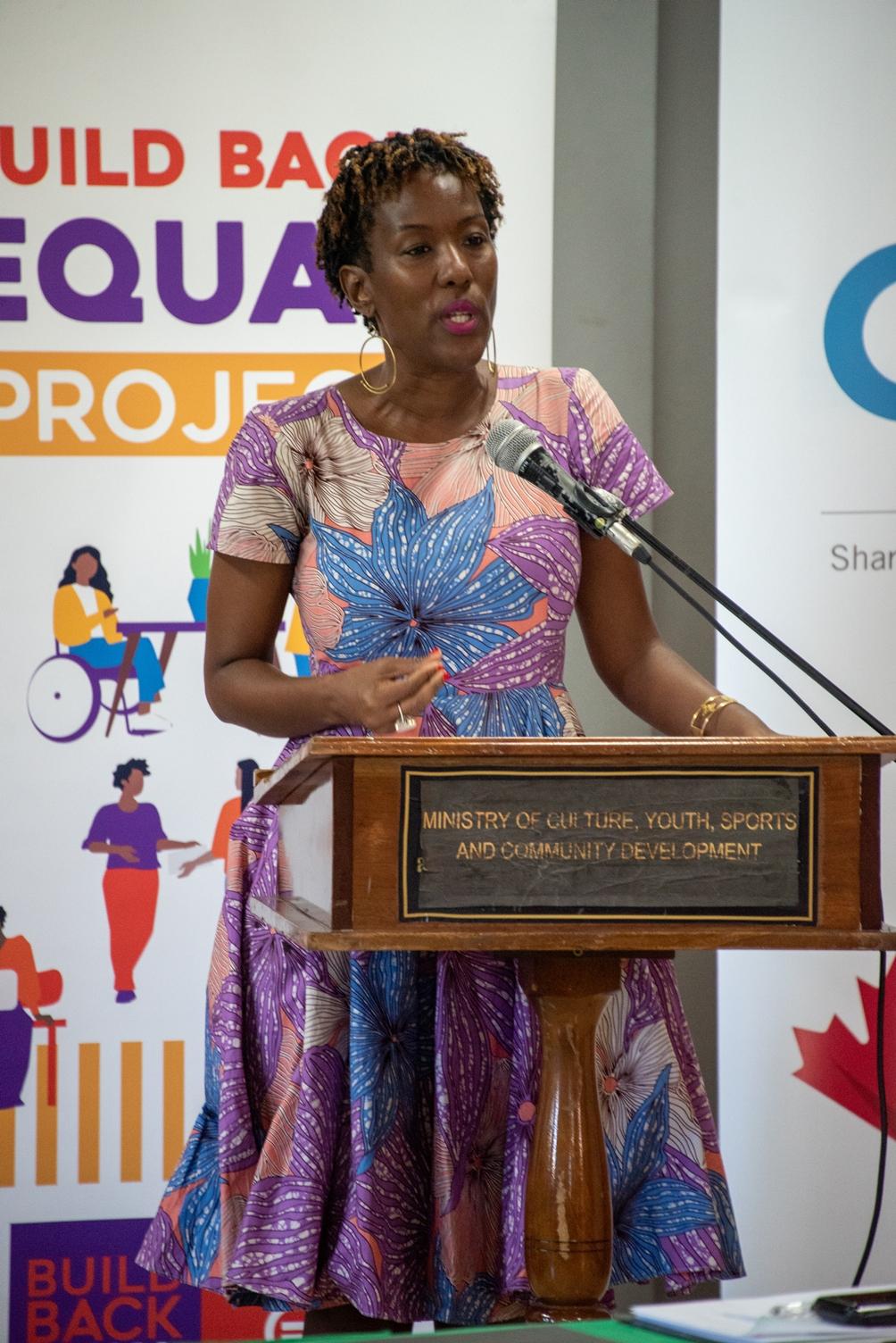 A woman standing at a podium in a dress with a banner behind her