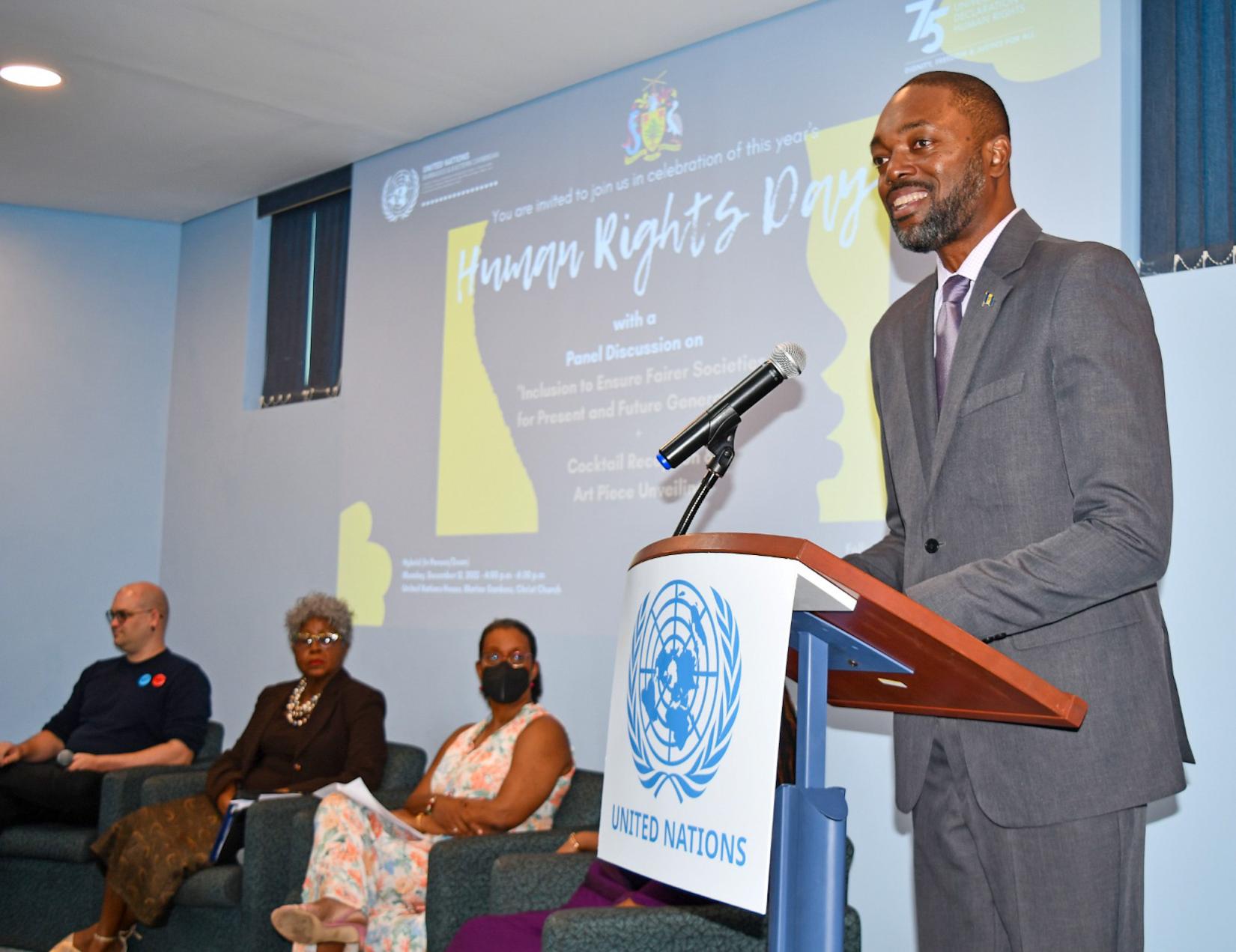 Minister of Labour, Social security and the Third Sector in Barbados, the Hon. Colin Jordan stands at the UN Podium on stage, delivering his featured address with the panel in the background, and the audience before him. 