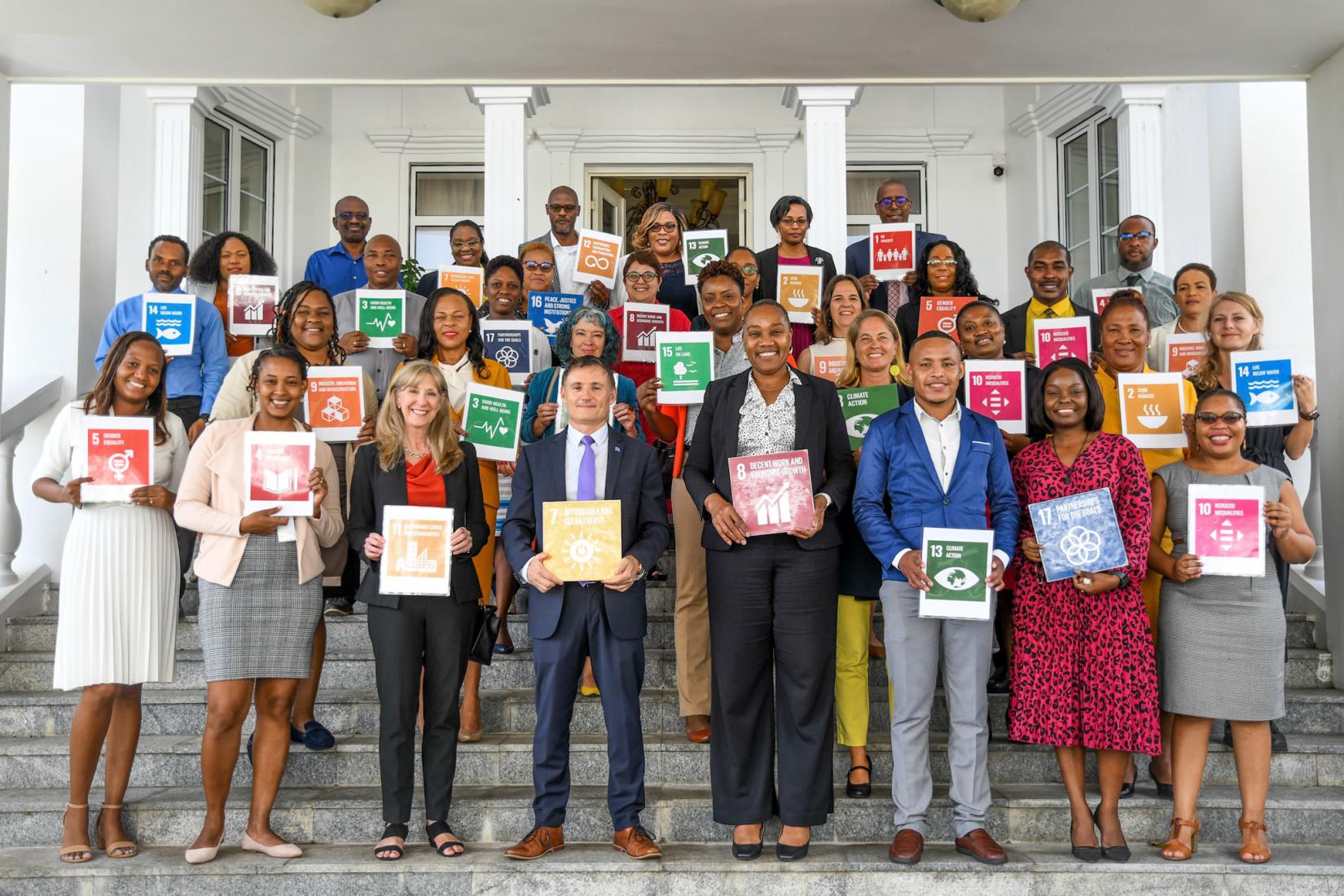 A group of people stand on stairs with SDG cards in their hands smiling for the camera