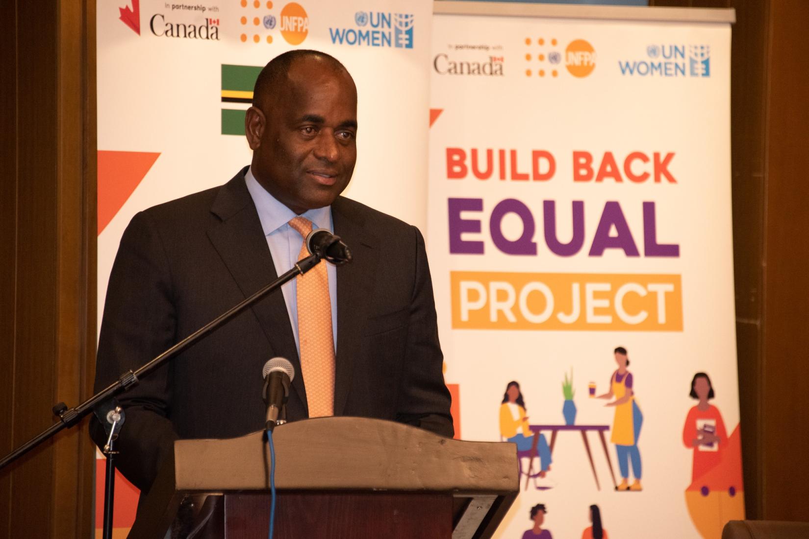 Man at podium speaks to an audience with banners in the background