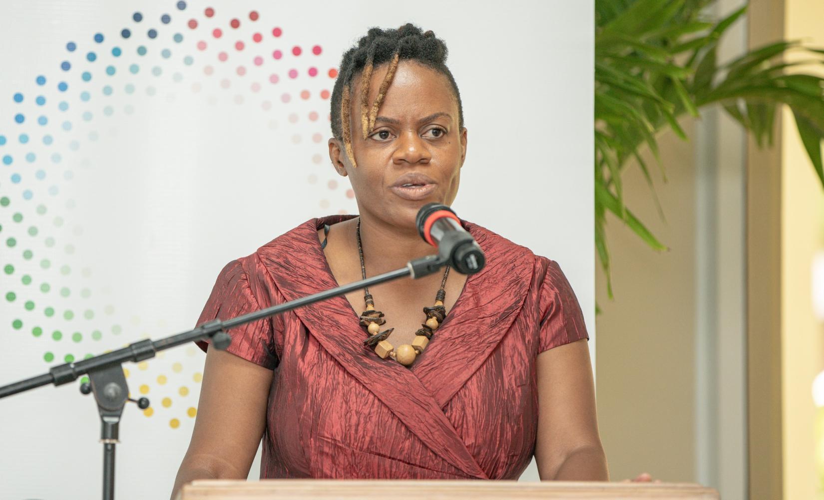 Woman at podium speaking into microphone to an audience with a banner behind her