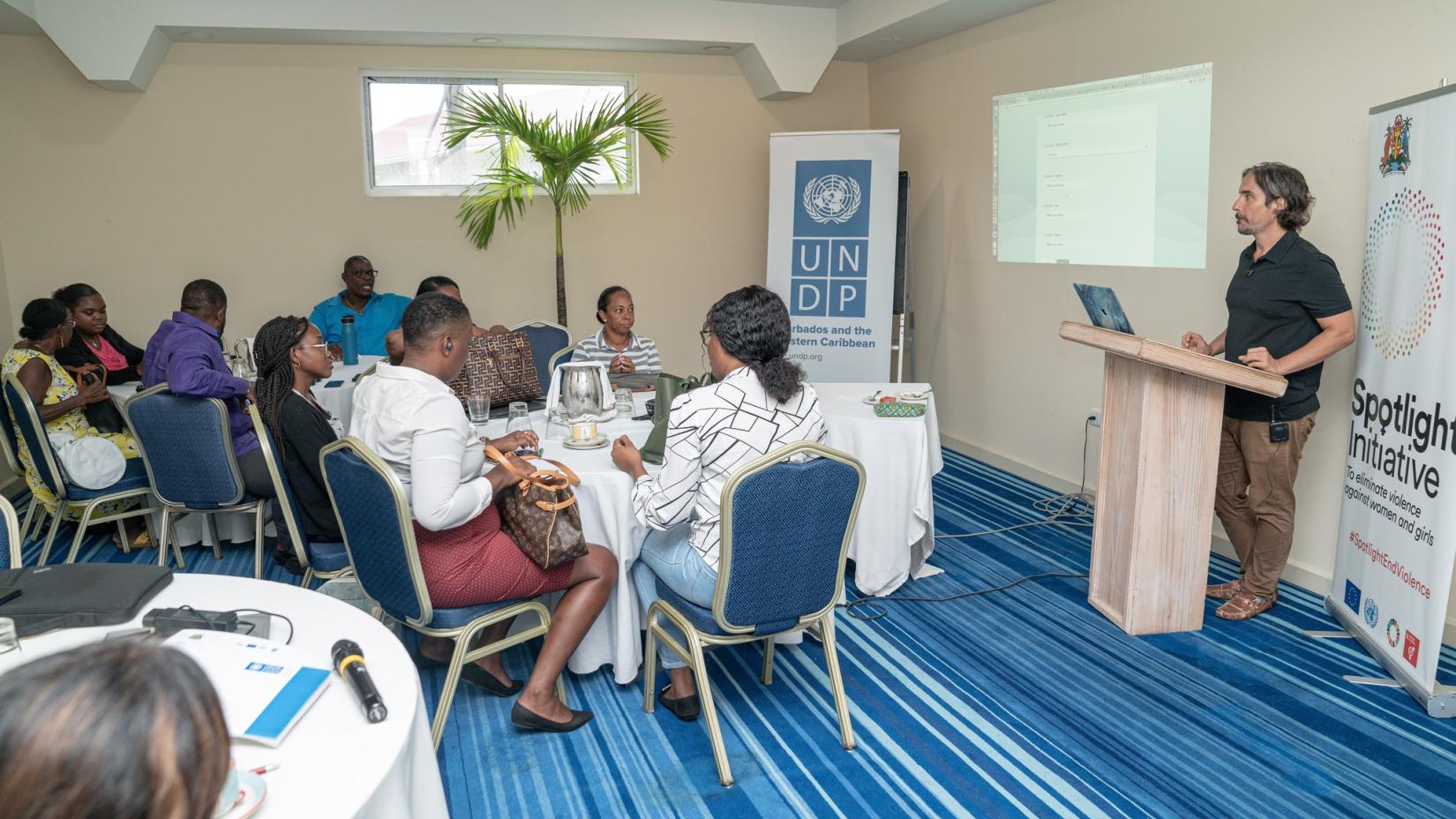 People sitting at tables around a room, paying attention to a man at a podium.