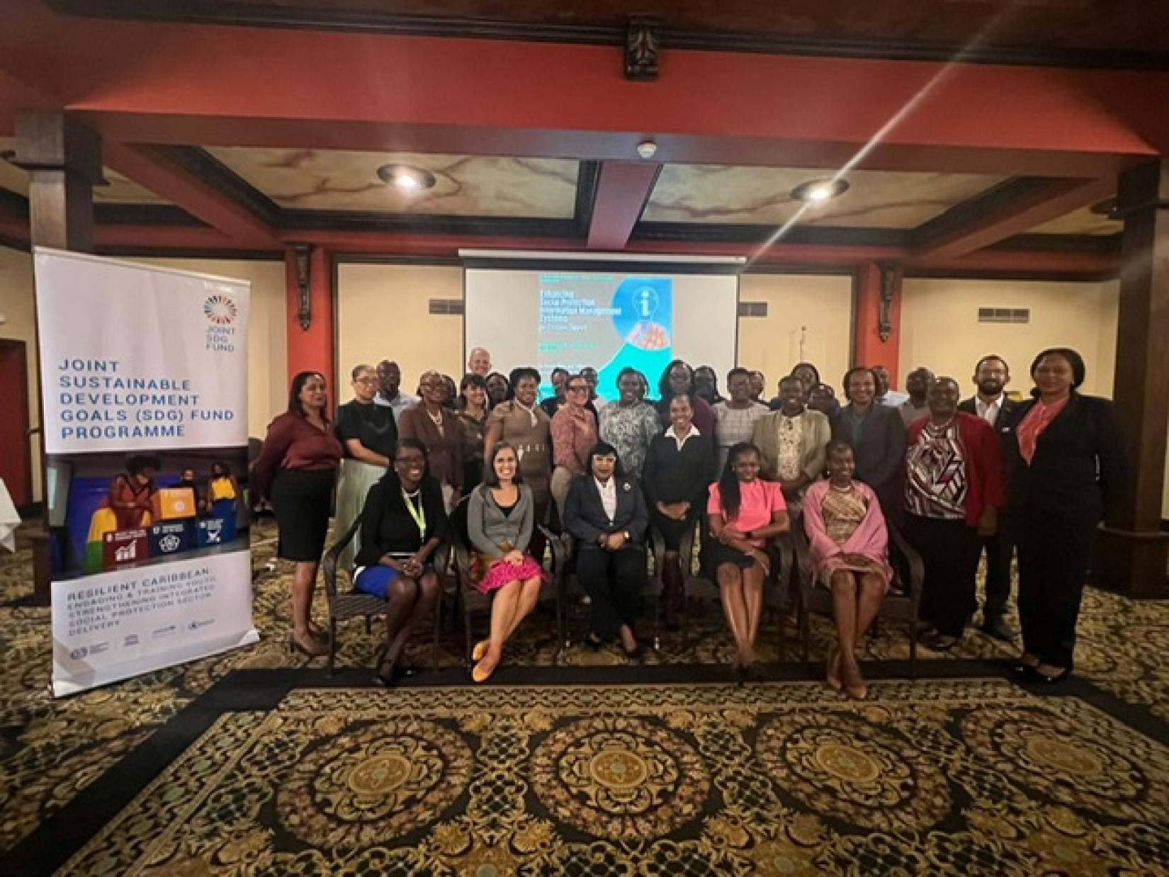 A group of persons sit down and smile for a group photo with the Joint SDG banner to their left