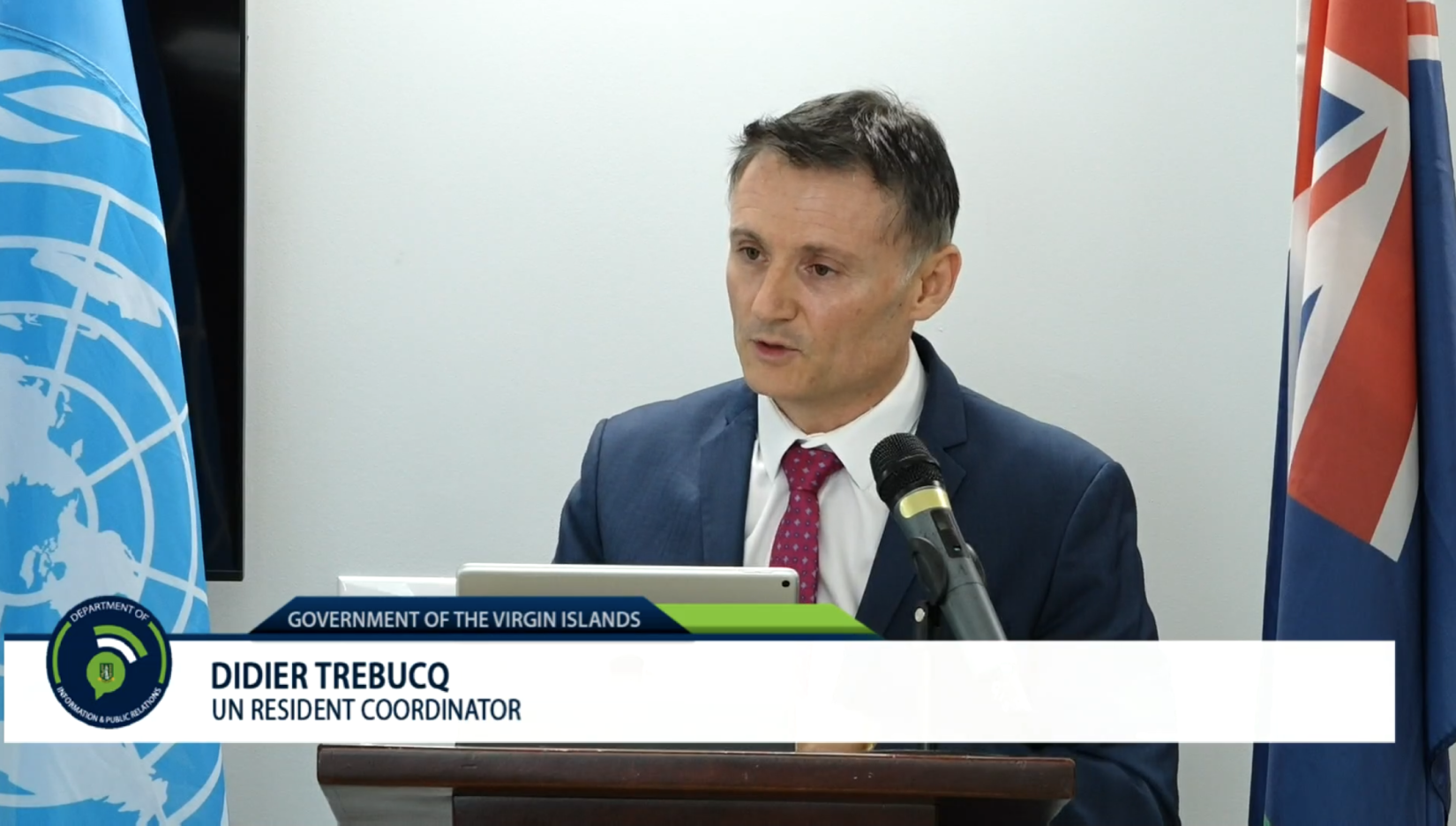 Screenshot of a man speaking in front of a podium with a lower third presenting