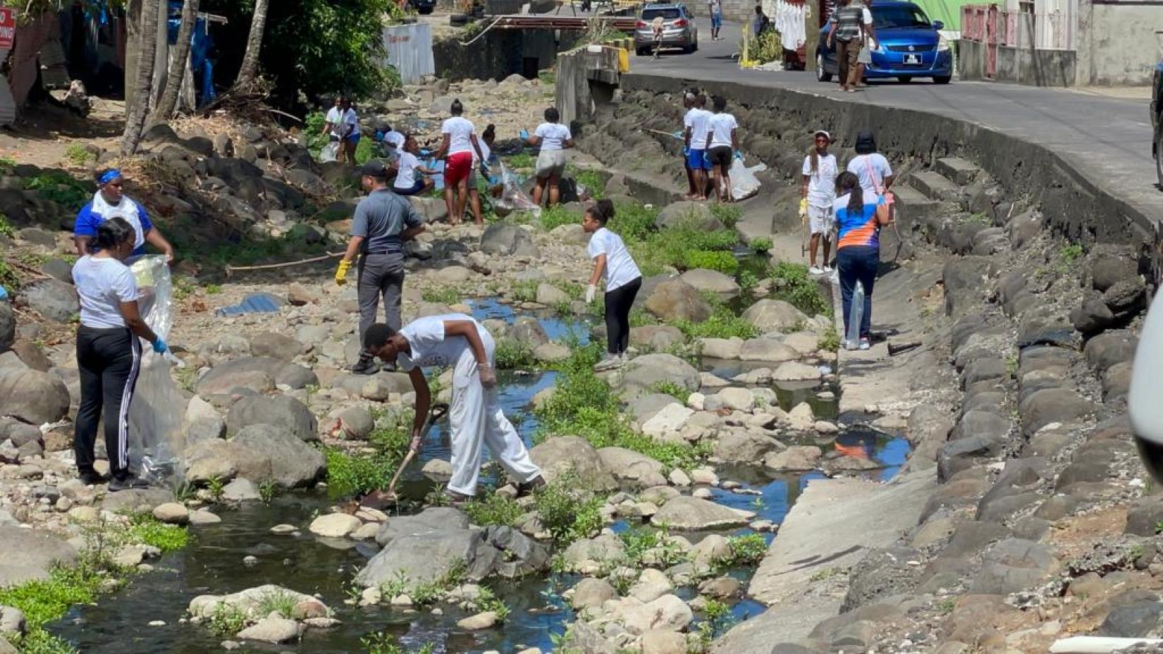 persons spread across a riverbed, collecting plastic waste