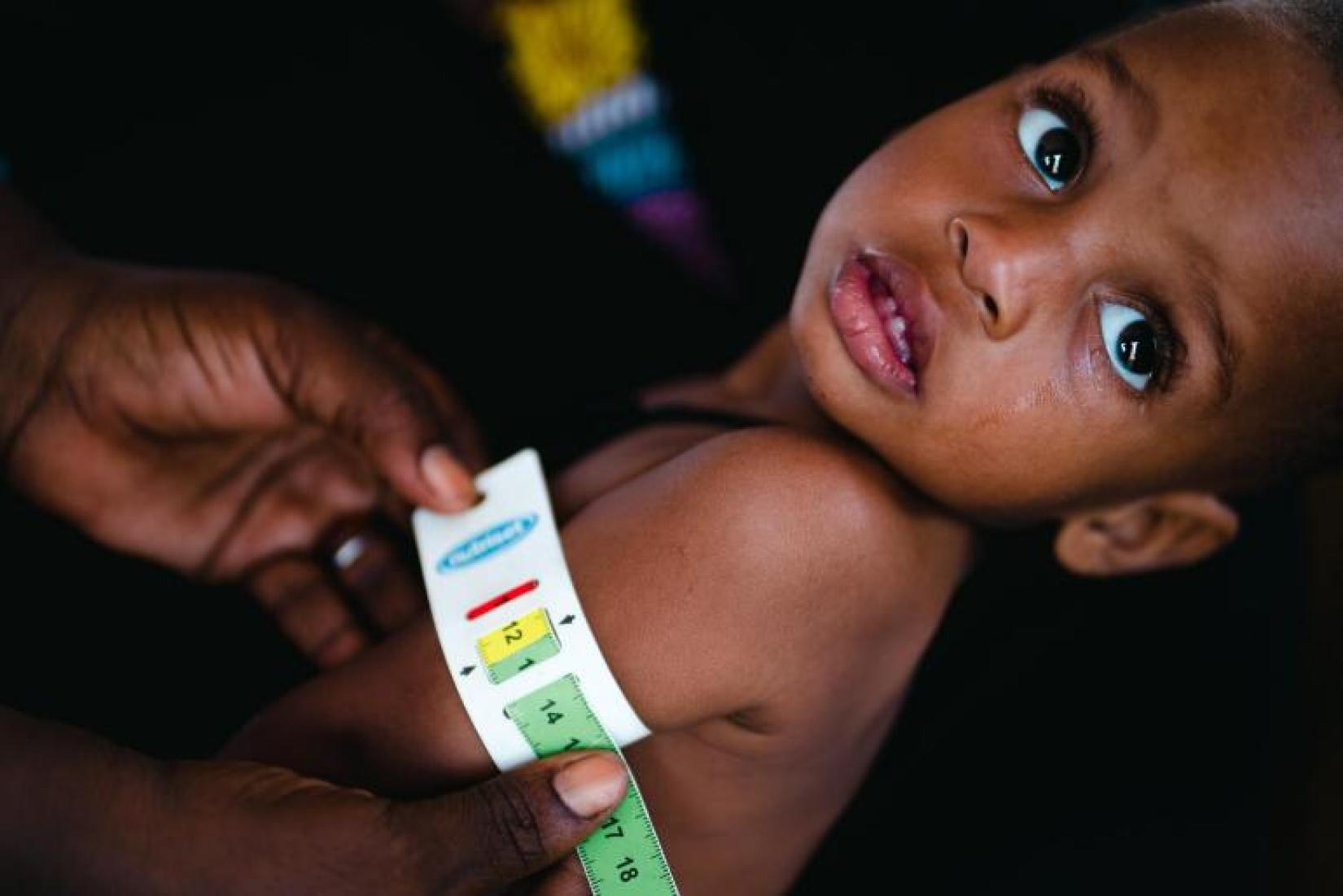 A child stays still to receive an arm measurement.