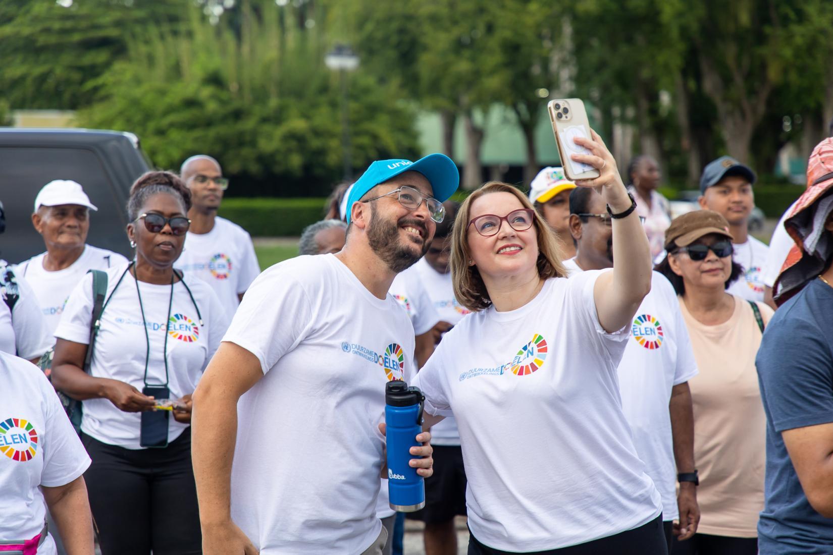 A woman raises an iPhone for a 'selfie' with a man while smiling in SDG shirts. 