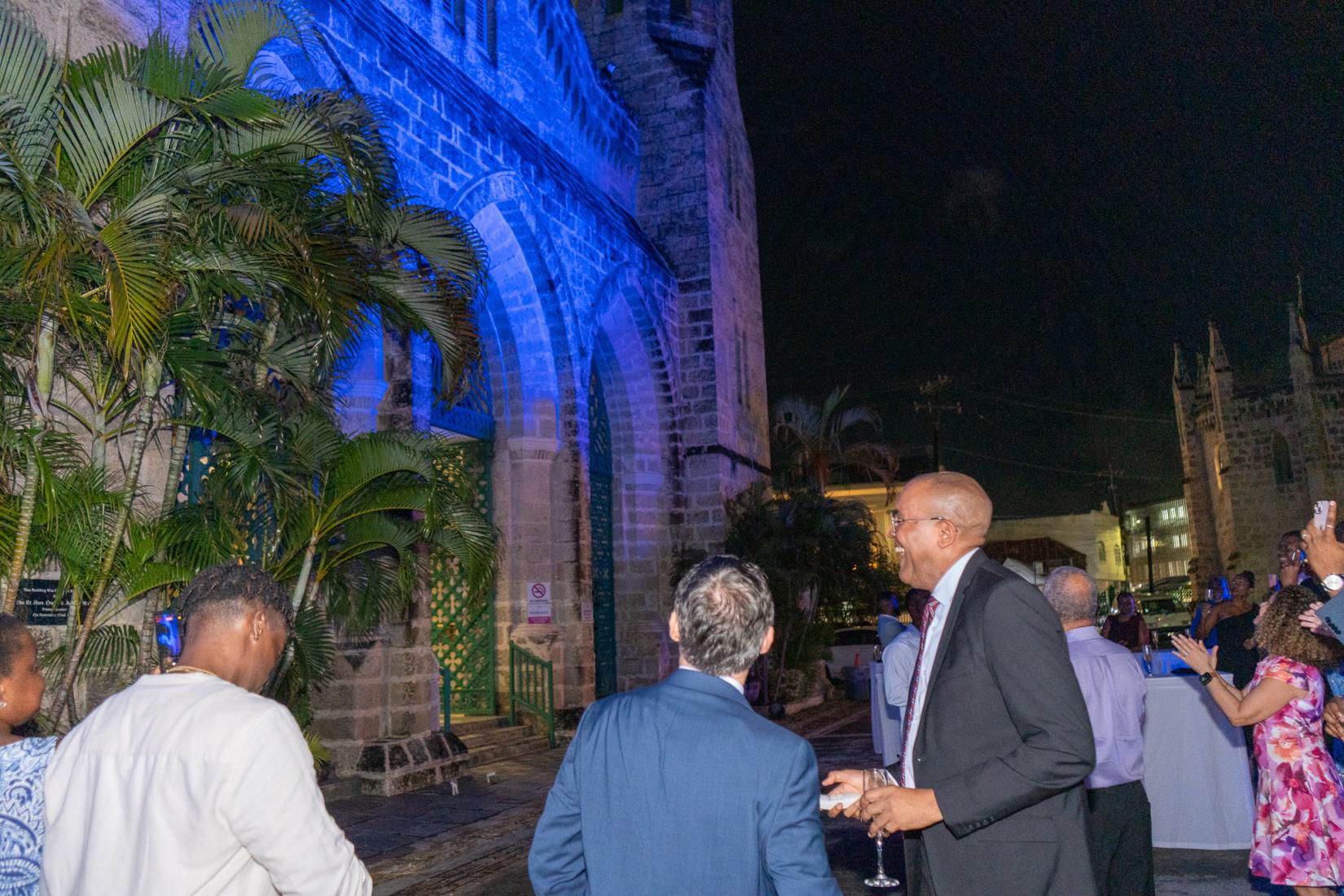 two men in suits stand facing a building lit in blue