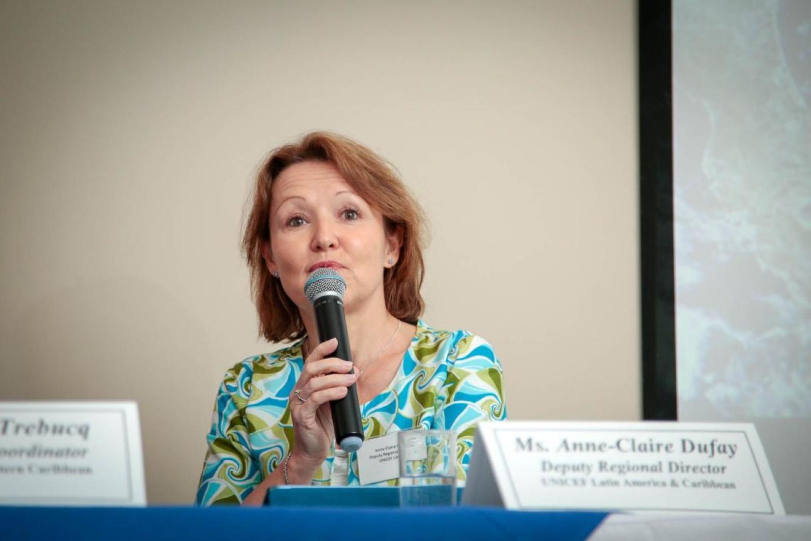 woman with microphone speaking from behind a table