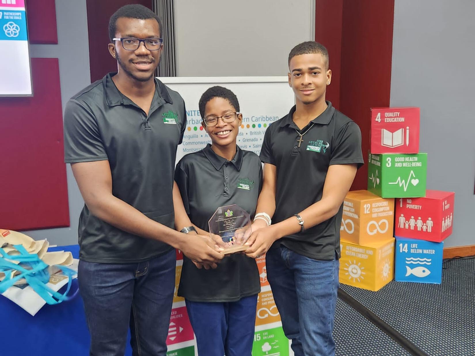 three young people hold an award together smiling with SDG blocks and an SDG banner in the background
