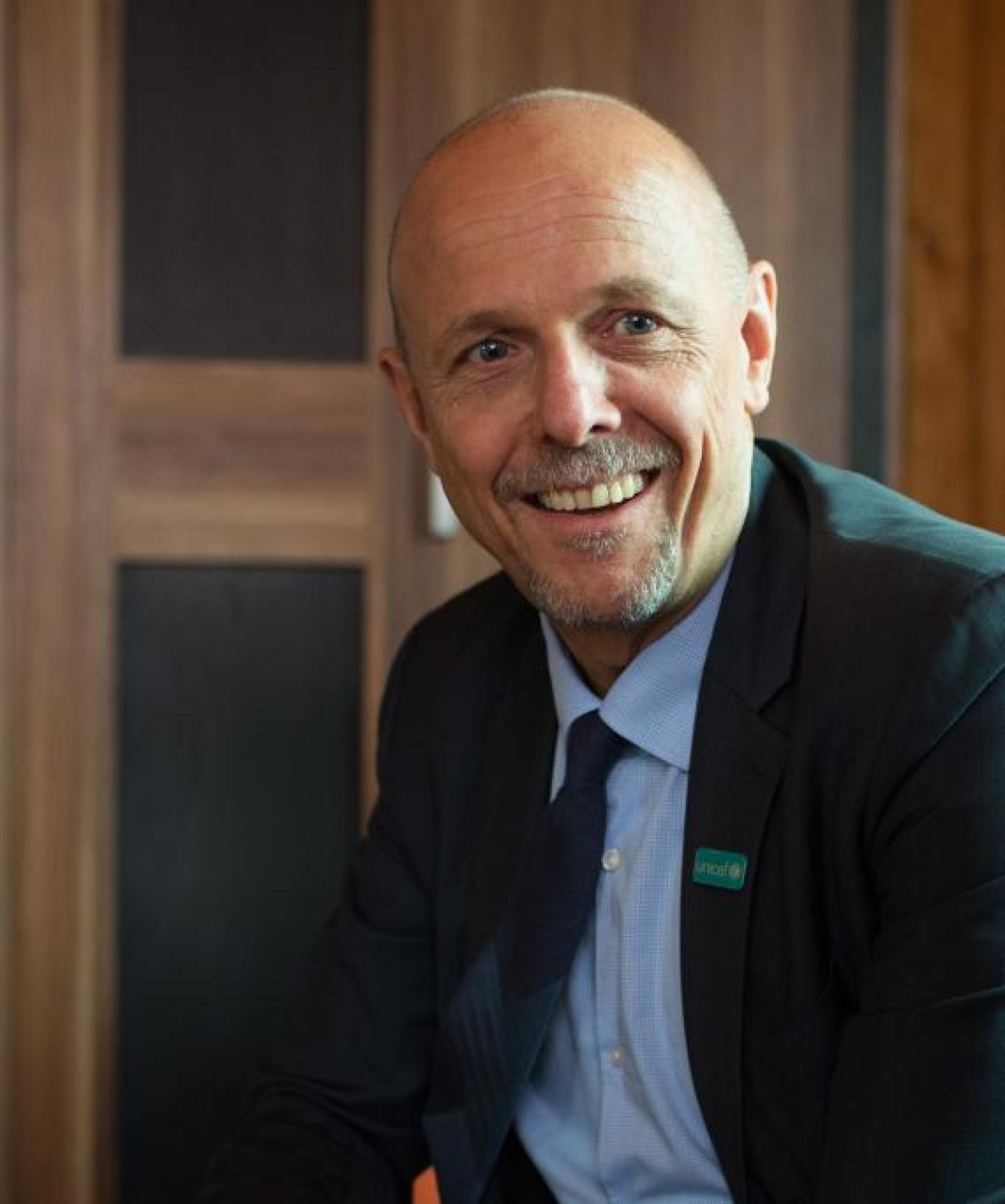 man in suit sits and shares a warm smile