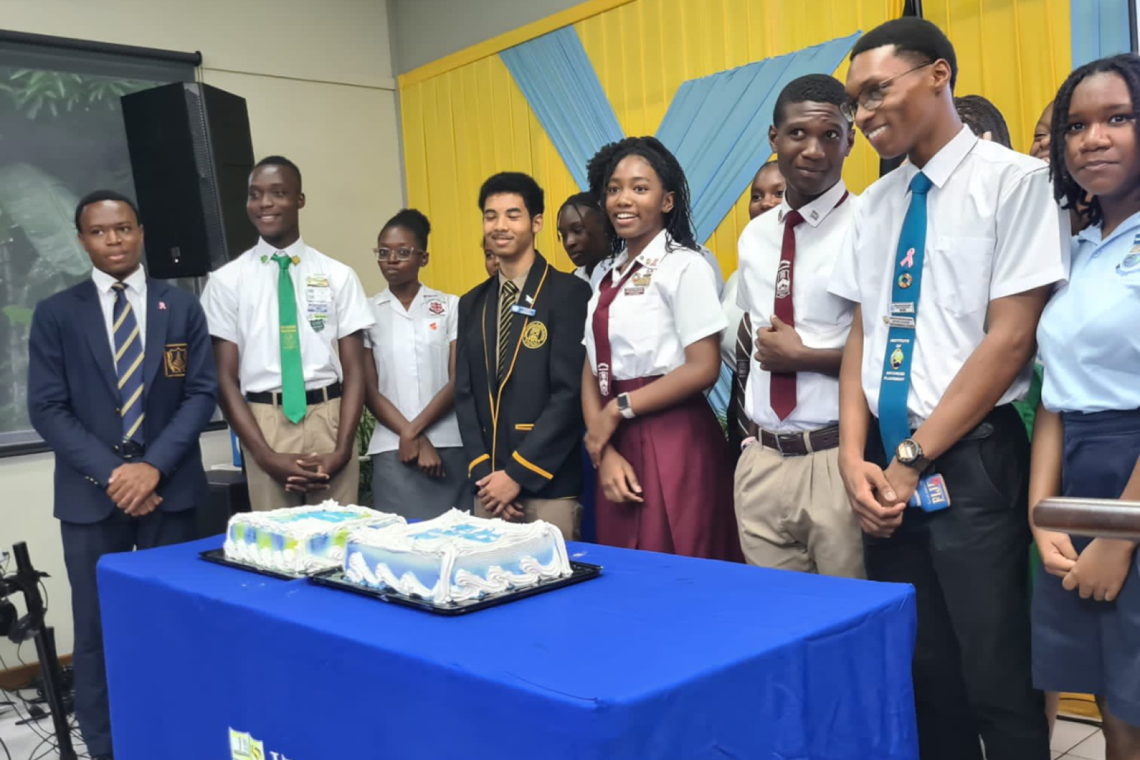 Young people gathered at Hillel Academy for a UN Day celebration featuring a special cake standing behind a table overlooking the cake