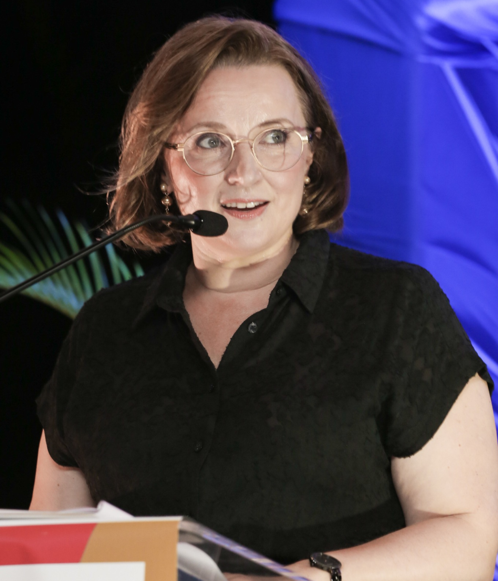 woman stands at podium with microphone and lights on her face