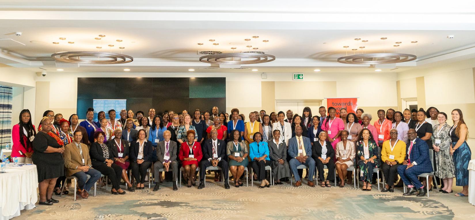 A group of people stand together for a photo, some sitting, some standing, in a wide photo of the room