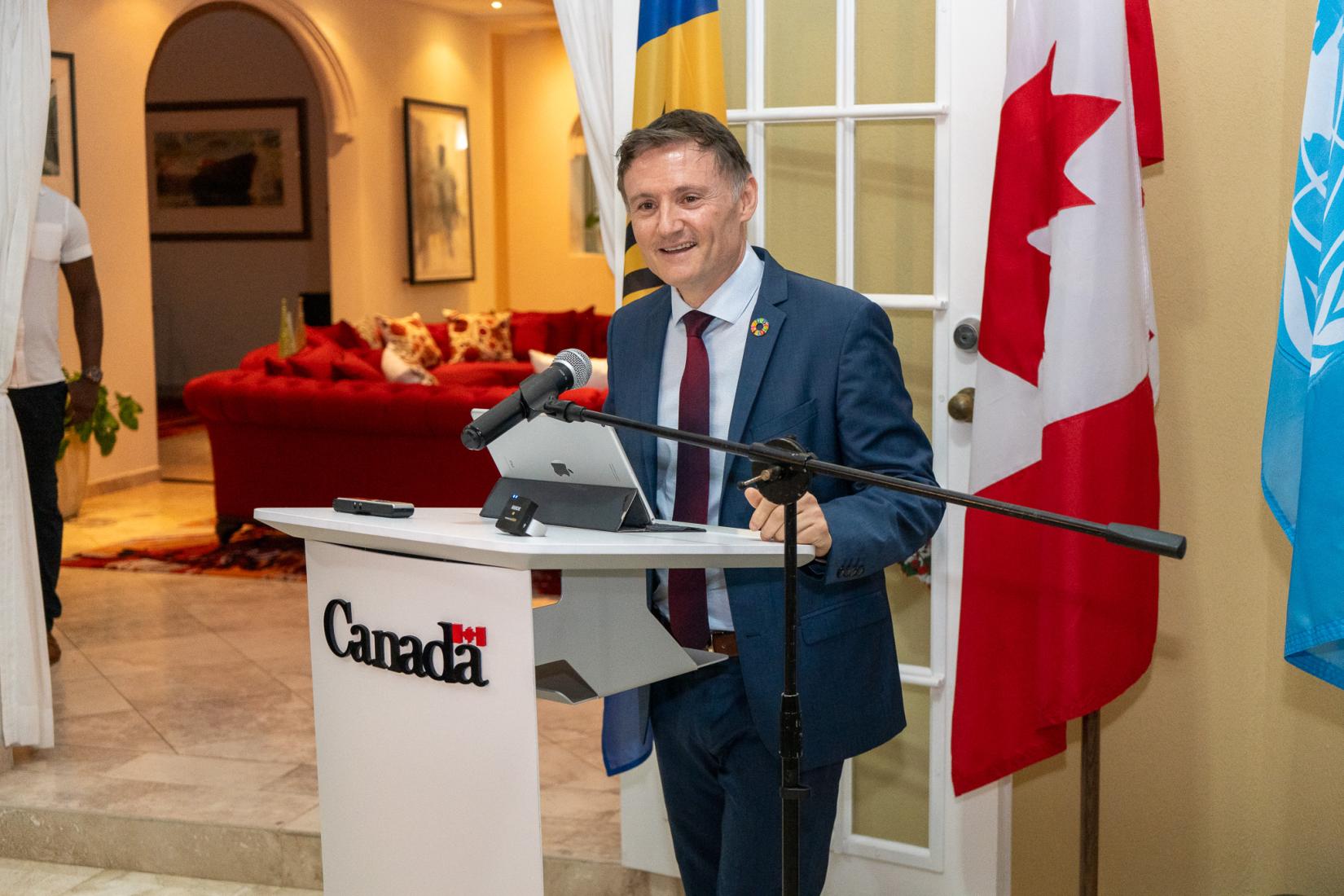 Man at podium speaks to an audience with flags in the background