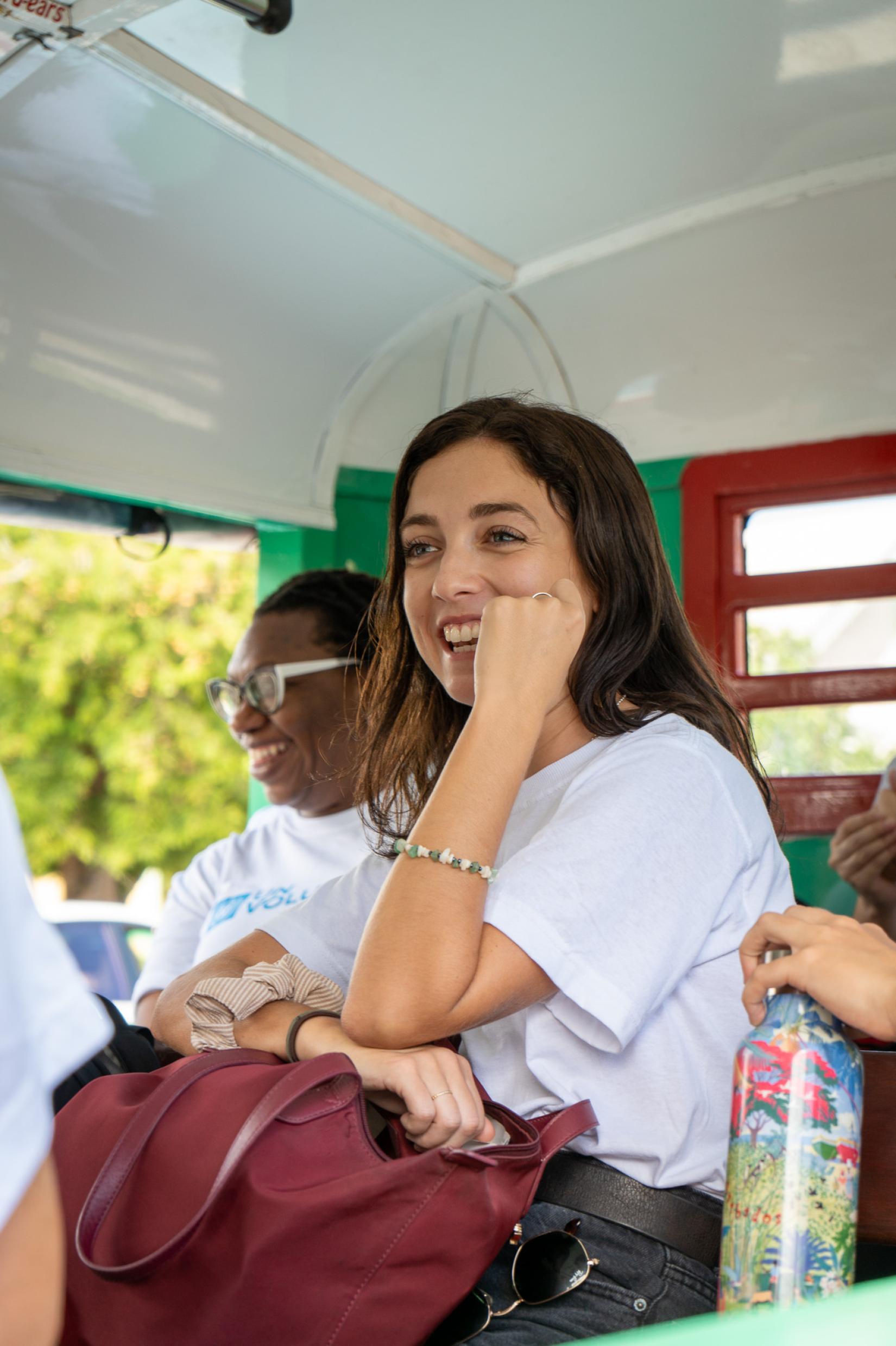 a woman in a white t shirt sits in a bus and smiles during conversation 