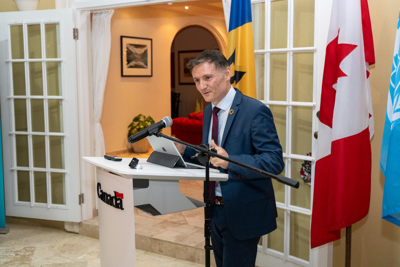 Man at podium speaks to an audience with flags in the background