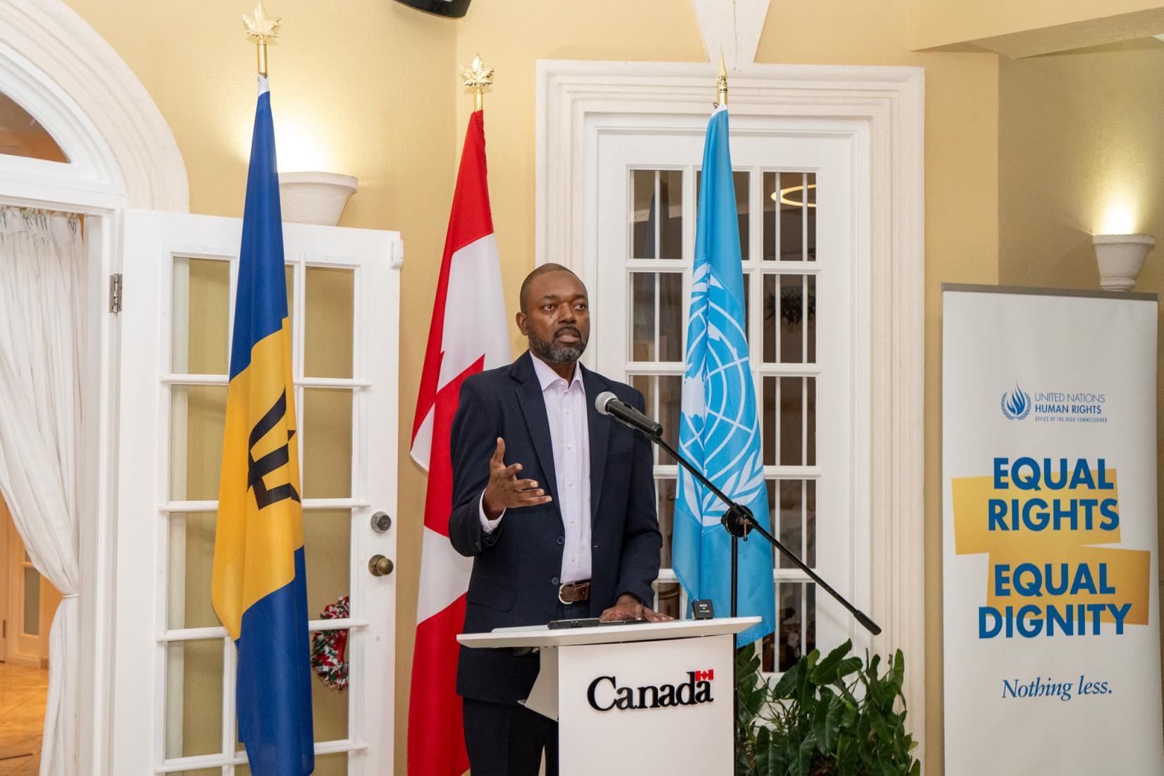 Man at podium speaks to an audience with flags in the background