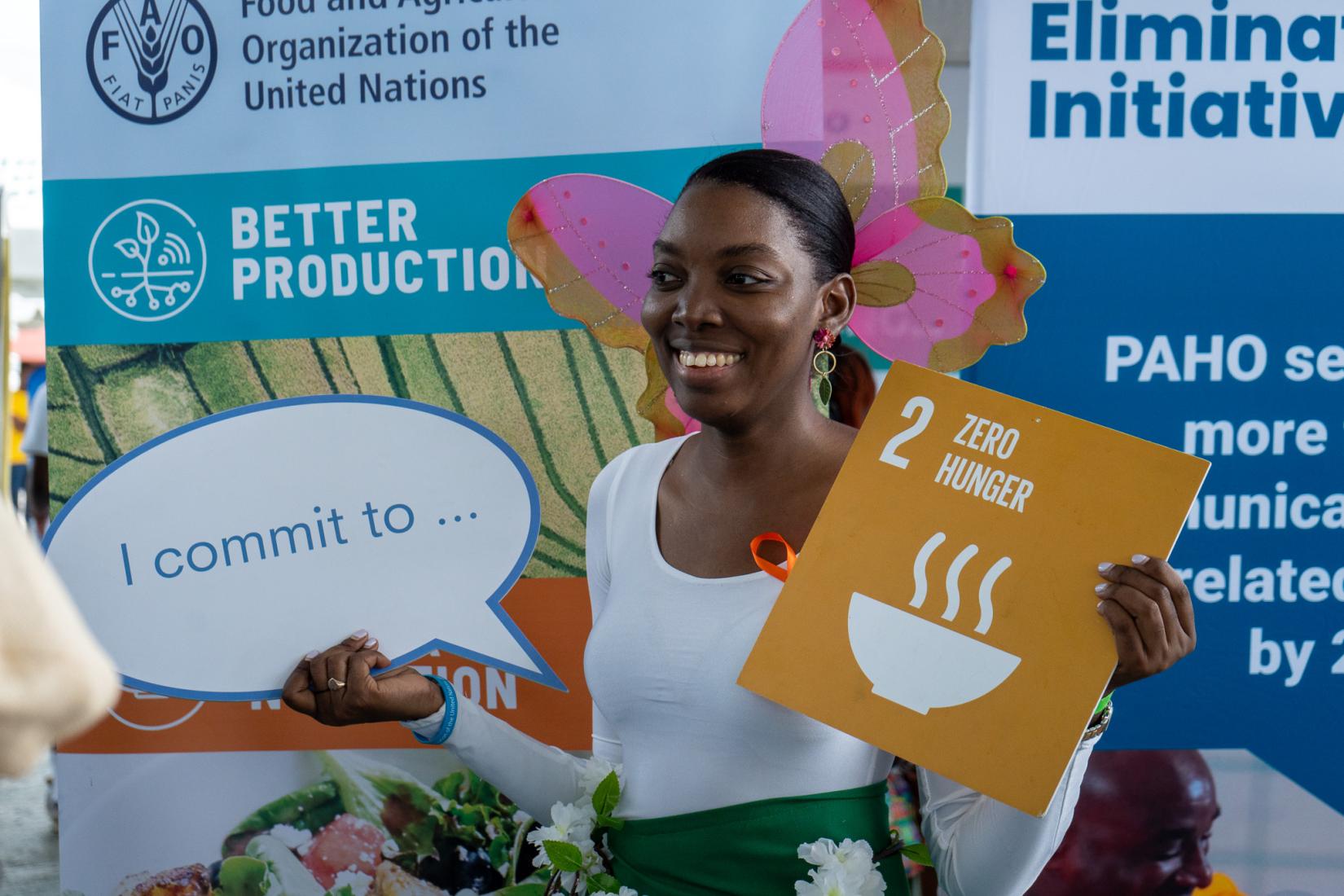 smiling woman in costume with butterfly attachment holding signs which say I commit to SDG 2 Zero Hunger