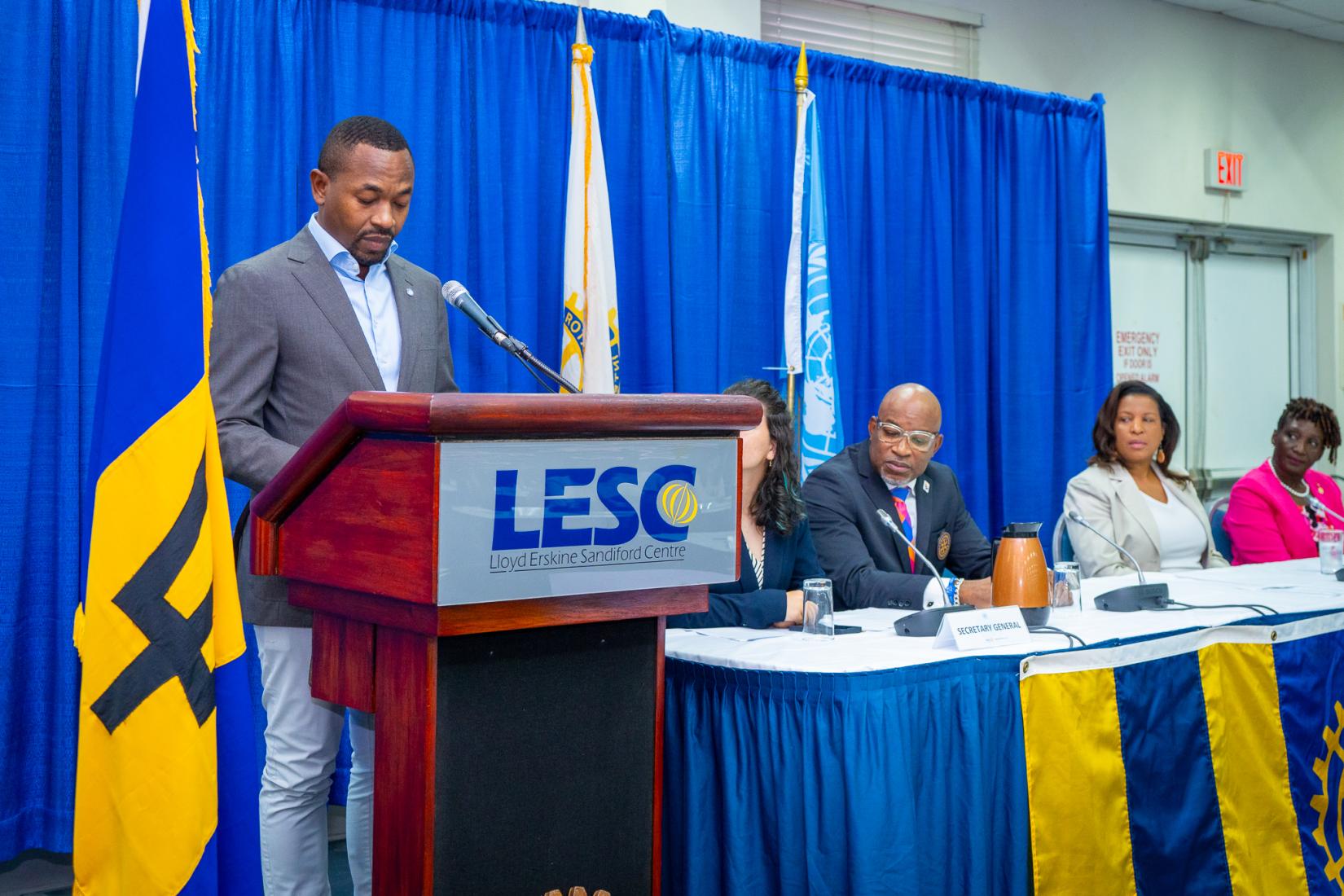 A person standing at a podium with a microphone and people behind him