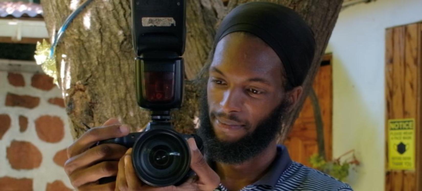 A young man holding a camera, and twisting the zoom on the lens