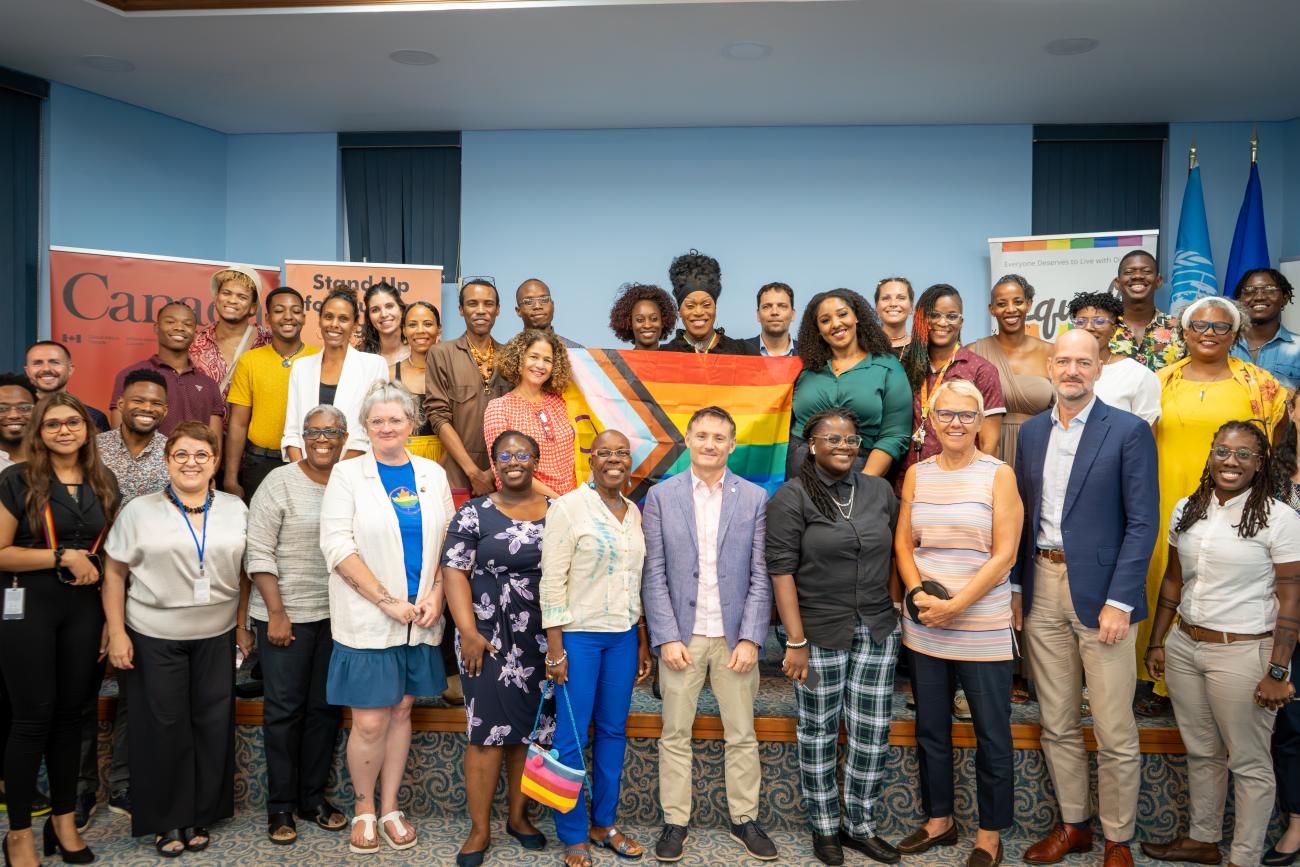 A large group of people standing together holding an LGBTI+ flag and smiling for a photo