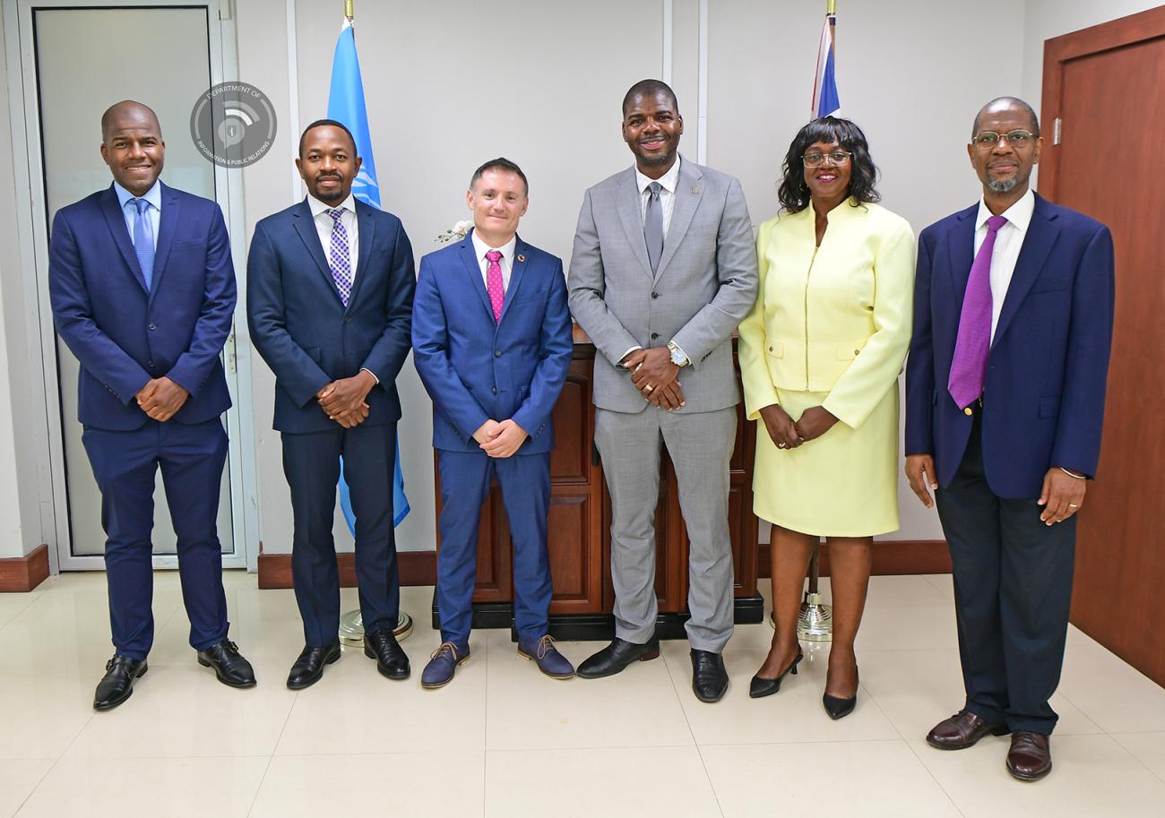 Group of UN and BVI Government officials stand with their hands in front of them in business attire; five men, and one woman.