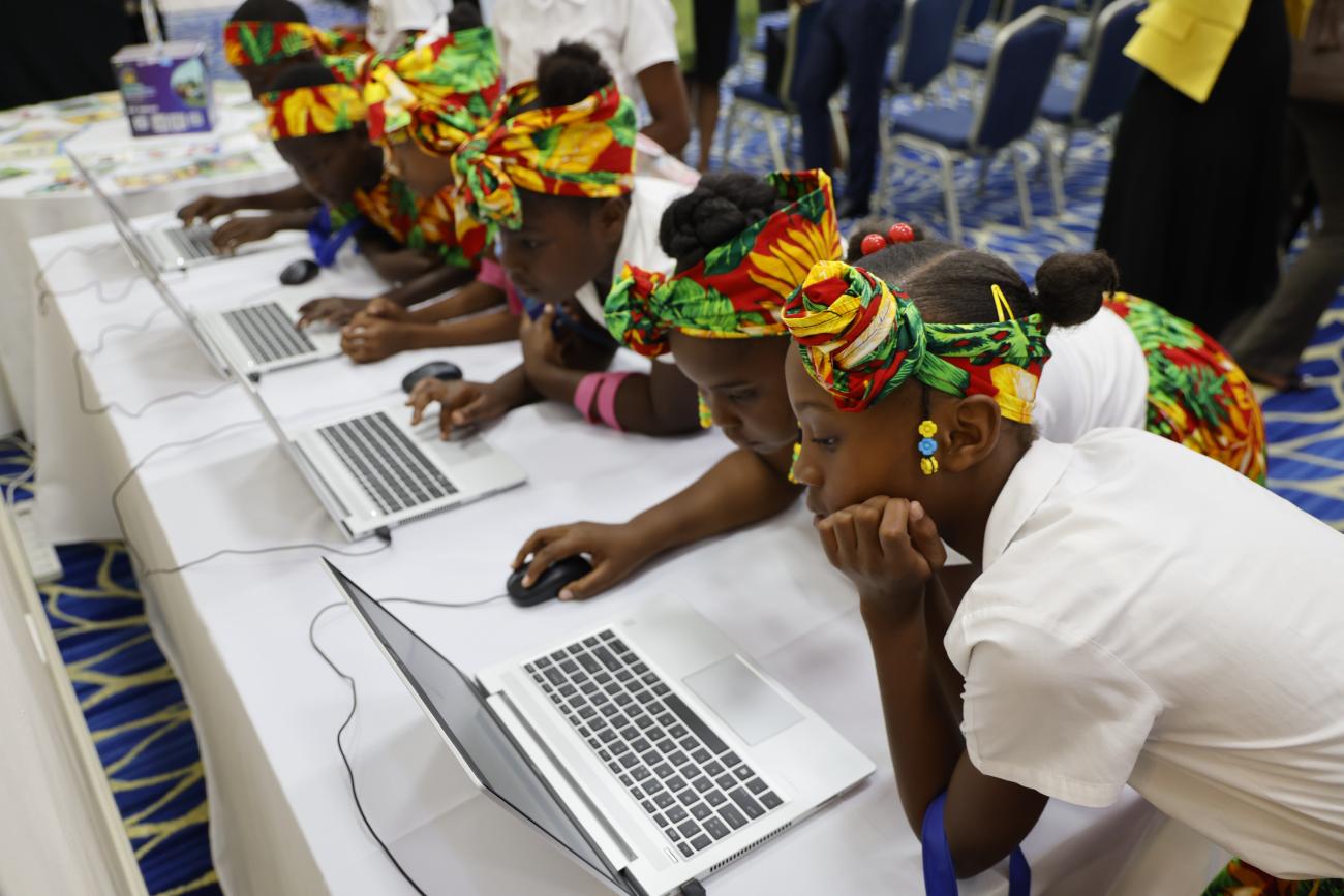 A row of students lean over to use their laptops across a long table