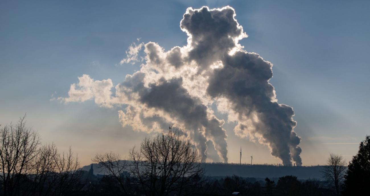 huge smoke plumes rising from a factory in the distance at sunset