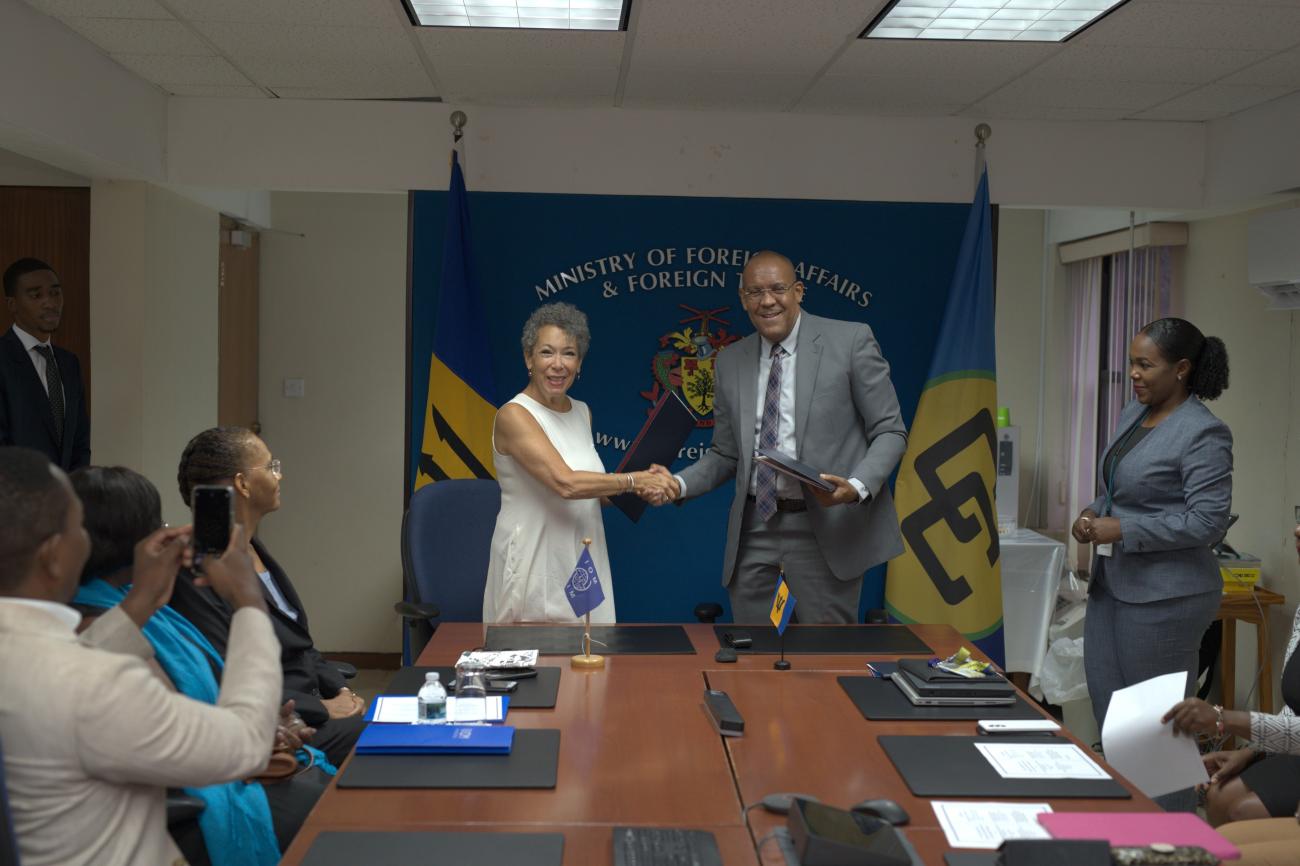 Man and woman exchange folder in a boardroom to a small gathering