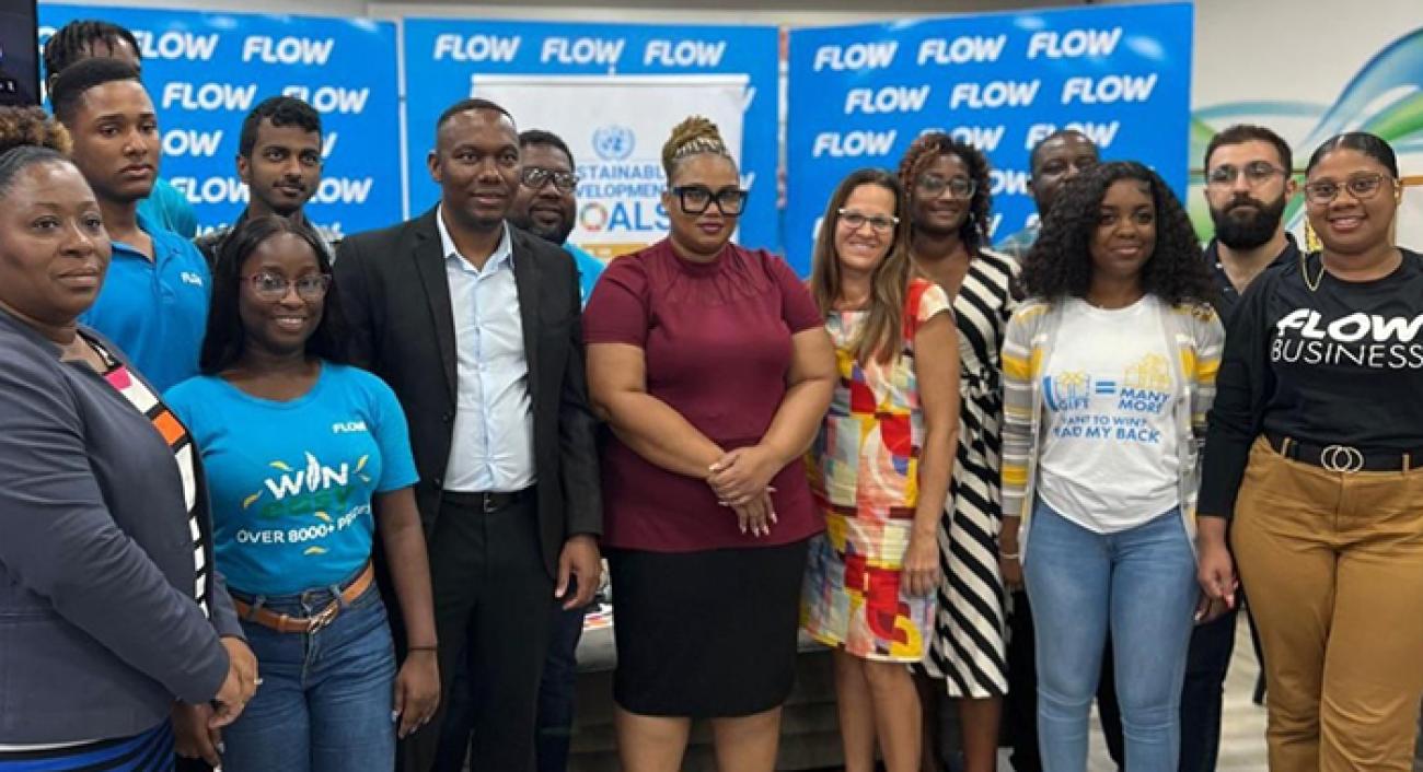 A group of 14 people stand together smiling for a photo with banners behind them