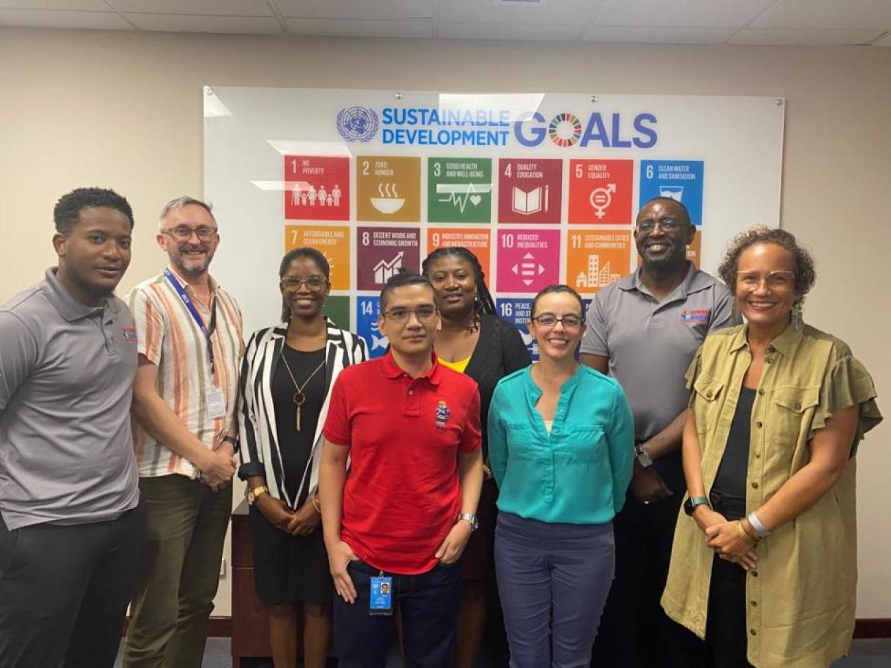 A group of people stand together for a photo in front of a poster of the SDGs. 