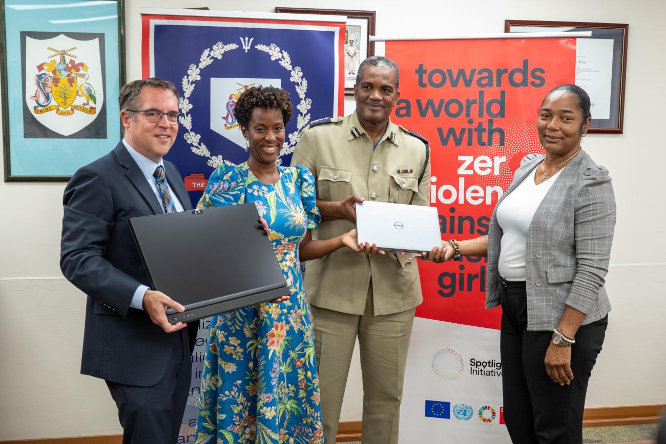 two men and two women stand together holding a laptop and a screen in front of banners