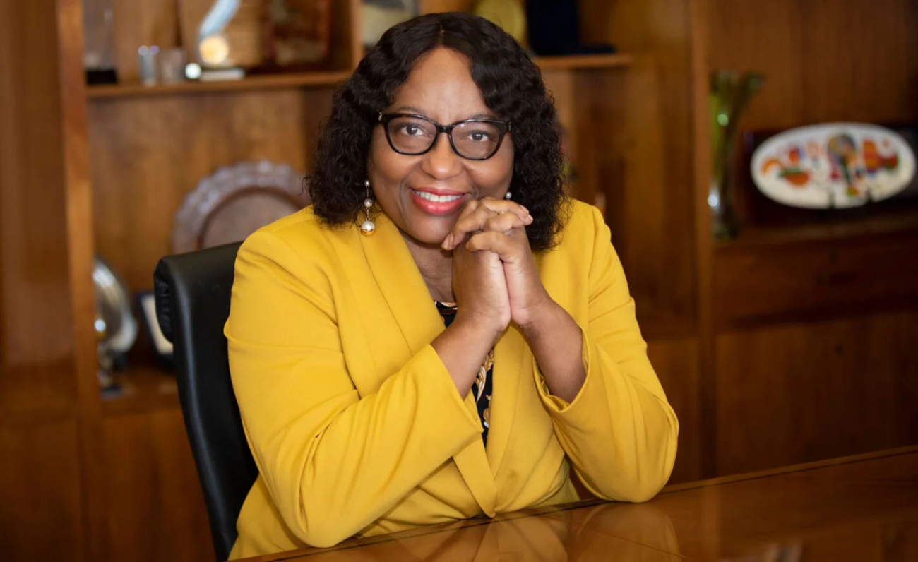 a lady in glasses poses for a picture smiling with her hands clasped on her face