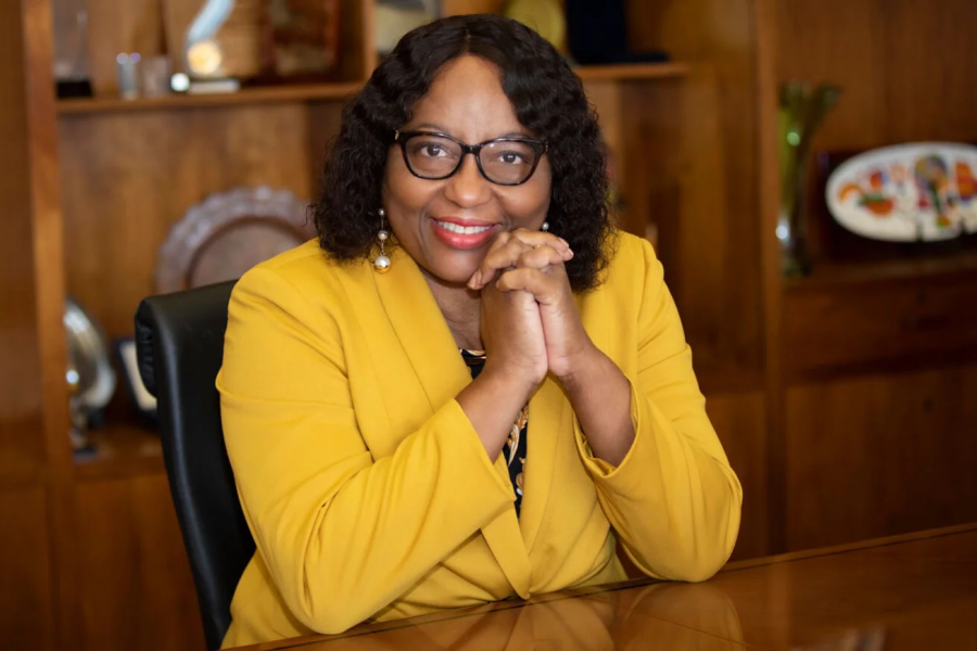 a lady in glasses poses for a picture smiling with her hands clasped on her face
