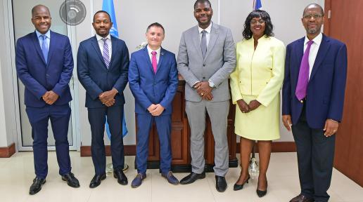 Group of UN and BVI Government officials stand with their hands in front of them in business attire; five men, and one woman.