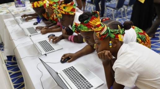 A row of students lean over to use their laptops across a long table