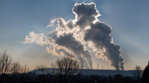huge smoke plumes rising from a factory in the distance at sunset