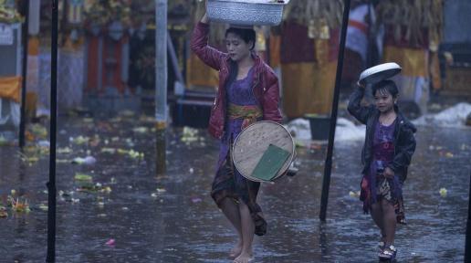 A mother and her daughter try to shield themselves from rain as they walk in a market.