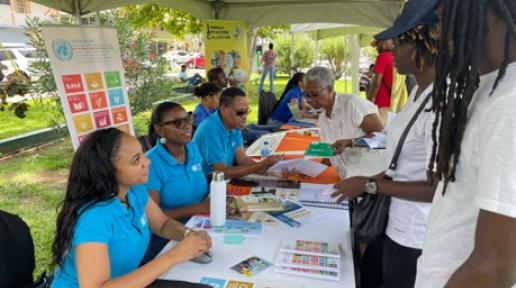 UN Team members sit behind a table backed by an SDG poster interacting with members of the public standing before them.