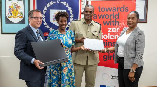 two men and two women stand together holding a laptop and a screen in front of banners