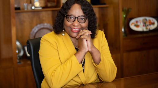 a lady in glasses poses for a picture smiling with her hands clasped on her face