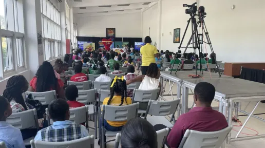 children sit in a hall facing a stage