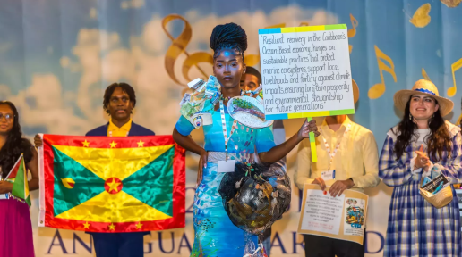 a girl in coastal themed fashion costume holding up a sign on a stage in front of other costumed youth