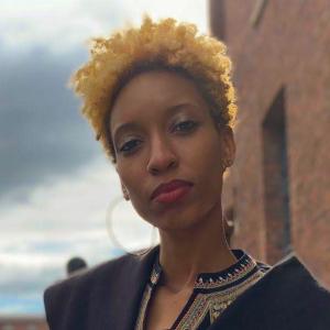 blurry headshot portrait of woman standing before a brick wall