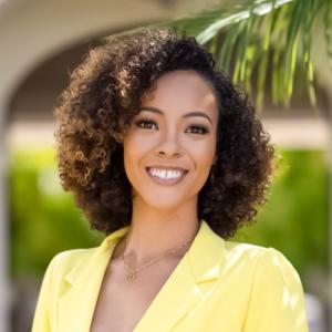 headshot of a smiling woman with curly hair in a yellow suit jacket