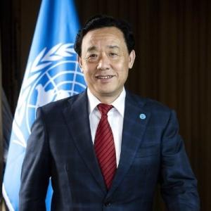 A person in a suit and tie with UN Flag in the background